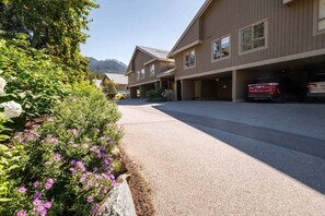 A building with a parking garage, a driveway, and a mountain in the background. - Townhome | Pets | BBQ | Free park | SmartTV | Wifi (Whistler)