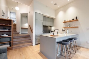 A modern kitchen with a central island, bar stools, and a staircase leading to another level. - Townhome | Pets | BBQ | Free park | SmartTV | Wifi (Whistler)