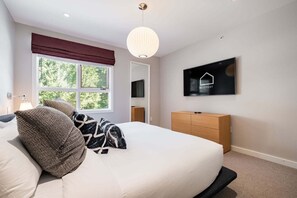 A bedroom with a bed, a television on the wall, a window with a view of trees, and a wooden dresser. - Townhome | Pets | BBQ | Free park | SmartTV | Wifi (Whistler)