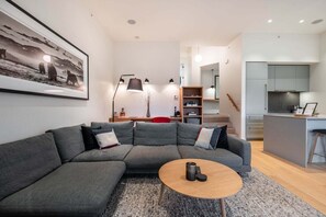 A modern living room with a sectional sofa, a coffee table, and a kitchen area in the background. - Townhome | Pets | BBQ | Free park | SmartTV | Wifi (Whistler)