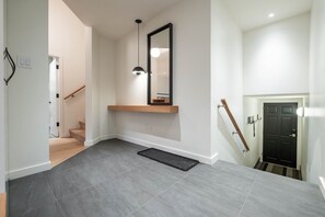 Ein moderner Flur mit einer Holztreppe, einer schwarzen Tür und einem an der Wand befestigten Spiegel.