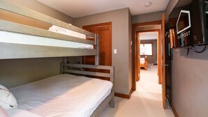 Quarto com beliches, televisão e porta que dá para outro cômodo.