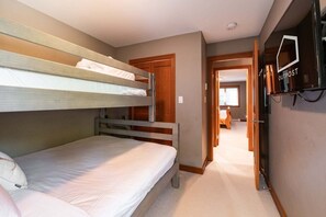 A room with bunk beds, a television, and a door leading to another room. - Townhome | Complex hot tub | BBQ | Free Parking (Whistler)