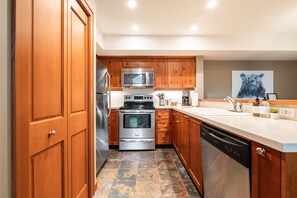 A modern kitchen with wooden cabinets, stainless steel appliances, and a tiled floor. - Townhome | Complex hot tub | BBQ | Free Parking (Whistler)