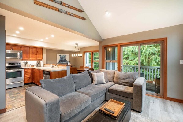 A modern kitchen with built-in appliances, a dining area with a large window, and a gray sectional sofa. - Townhome | Complex hot tub | BBQ | Free Parking (Whistler)