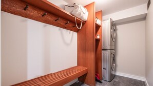 Una lavanderia con lavatrice, una panca e uno scaffale in legno con ganci.