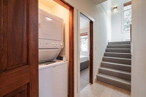Ein Waschraum mit Waschmaschine und Trockner, einer Holztür und einer Treppe, die zu einem Schlafzimmer mit Fenster führt.