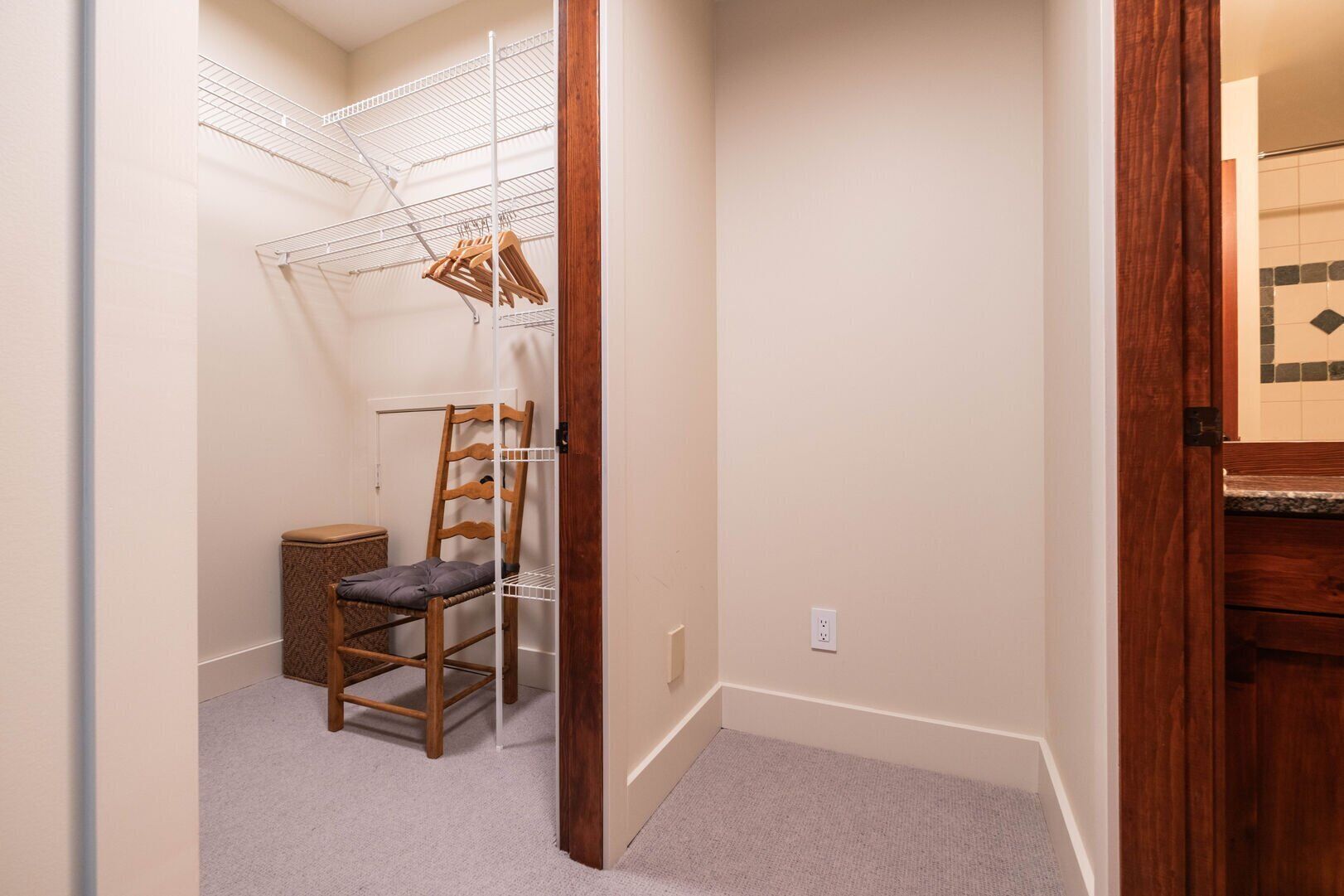 Un couloir étroit avec une chaise en bois, une étagère en métal et un petit panier en osier.