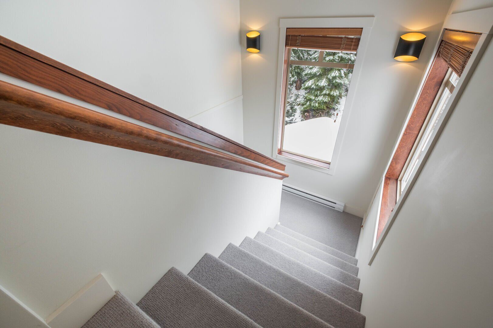 A staircase with wooden handrails and carpeted steps leading to a window with a view of trees.