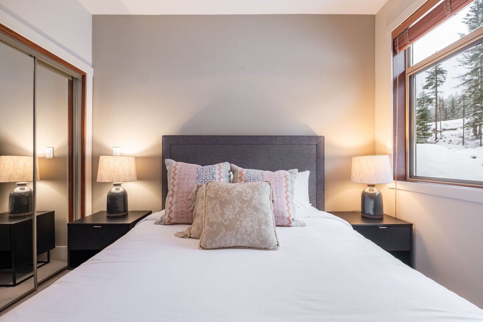 Een hotelkamer met een groot bed, twee nachtkastjes met lampen, een hoofdeinde en een raam met uitzicht op sneeuw.