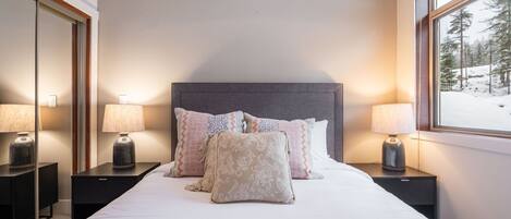 Quarto de hotel com uma cama grande, duas mesas de cabeceira com luminárias, cabeceira e janela com vista para neve.