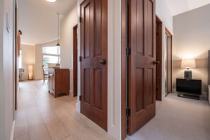 A spacious hallway with wooden doors, a dining area with a table and chairs, and a lamp on a side table. - Townhome | Wifi | Complex hot tub | BBQ (Whistler)