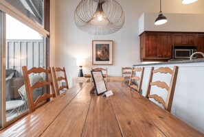 Ein Holzespeisesaal mit sechs Stühlen, einer Pendelleuchte, einem begrüßungsschild im Bilderrahmen sowie einer Küchenzeile mit Holzschränken und Geräten.