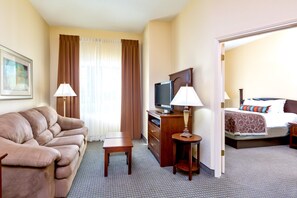 A hotel room with a sofa, a television, a desk, a lamp, and a bed with pillows.