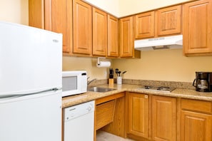A compact kitchen with wooden cabinets, a white refrigerator, a microwave, a dishwasher, a sink, and a coffee maker. - Chic 1BR Suite w/ Free Breakfast, Pool & Hot Tub (McAllen)