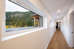 A modern interior with a long hallway, large windows, and a view of a forested area. - Gorgeous Chalet | Private hot tub | BBQ | WIFI (Whistler)