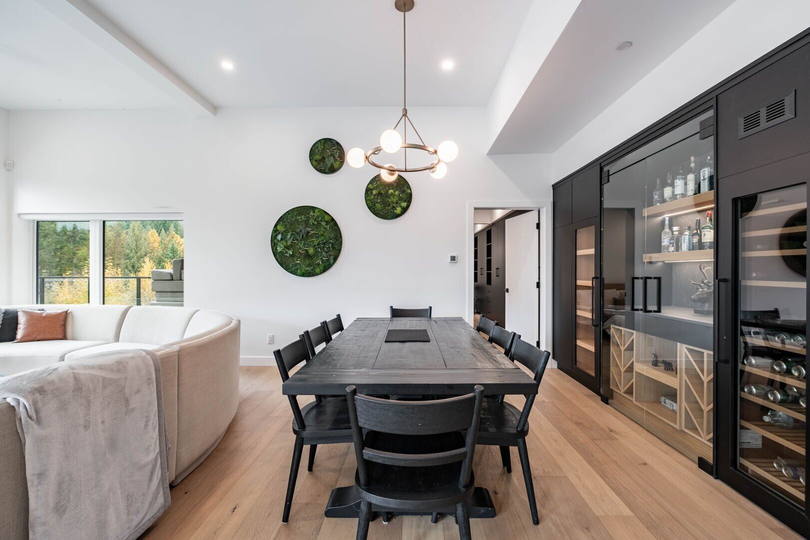 Une cuisine moderne avec un coin repas, comprenant une grande table en bois, des chaises noires et un lustre original.