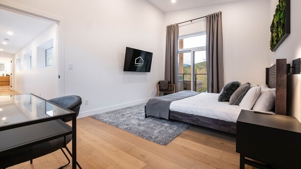Een moderne slaapkamer met een bed, een bureau en een aan de muur bevestigde televisie.