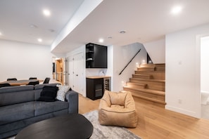 Een moderne woonkamer met een bank, een salontafel, een loungestoel, een eettafel met stoelen, een keuken en een trap.