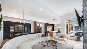 Een moderne woonkamer met een grote L-vormige hoekbank, een glazen salontafel en een keuken met donkere kasten en een bar.