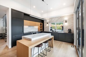 A modern kitchen with a marble countertop, dark cabinetry, and a large window. - Gorgeous Chalet | Private hot tub | BBQ | WIFI (Whistler)