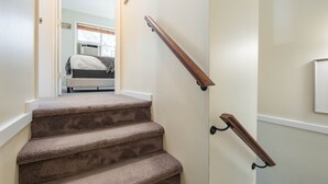 Ein Teppichbelag bedeckter Treppenaufgang mit hölzernen Geländern, der zu einem Schlafzimmer mit Bett und Fenster führt.