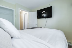Een slaapkamer met een bed, een aan de muur bevestigde televisie en een deur die naar een andere kamer leidt.