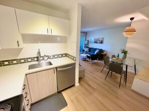 A modern kitchen with a dishwasher, a sink, and a dining area with a glass table and chairs. - Townhome | Private hot tub | Complex pool | BBQ (Whistler)