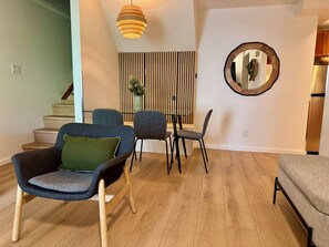 Een moderne woonkamer met een eethoek, met een trap, een houten vloer en een decoratieve spiegel.