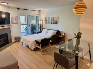 A modern bedroom with a bed, bedside tables, a TV, and a glass dining table. - Townhome | Private hot tub | Complex pool | BBQ (Whistler)