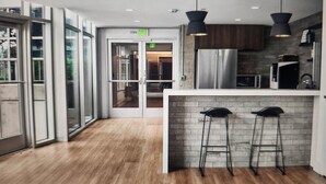 Una cocina moderna con refrigerador de acero inoxidable, piso de madera y taburetes negros.
