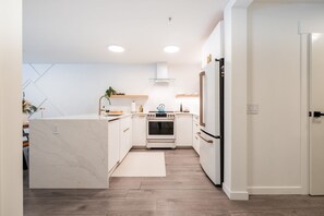 A modern kitchen with white cabinetry, a marble countertop, a built-in oven, and a refrigerator. - Free Parking | Blueberry Hill | Apple TV | Wifi (Whistler)