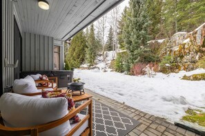 En mysig utomhusplats med sittmöbler, ett bubbelbad, trämöbler och ett snötäckt landskap med träd.