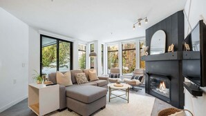 A modern living room with a sectional sofa, a fireplace, and large windows offering a view of the outdoors. - Free Parking | Private hot tub | Blueberry Hill (Whistler)