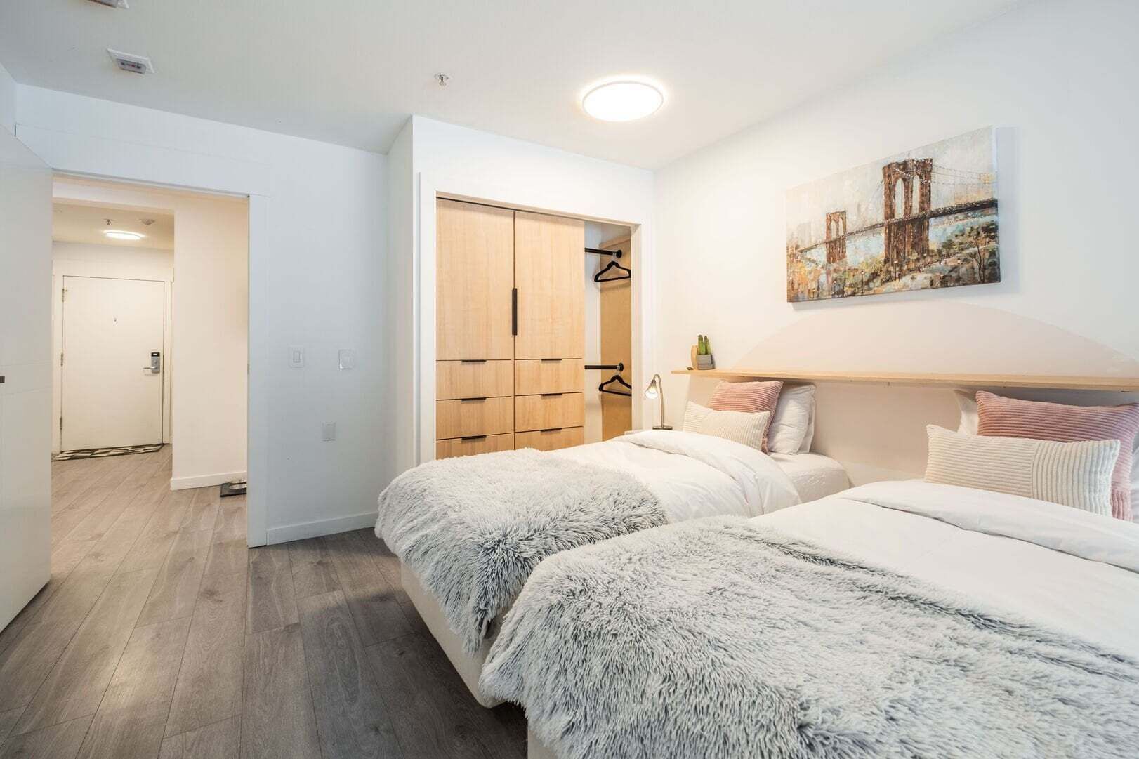Un dormitorio con dos camas, un armario, un cuadro y un pasillo.
