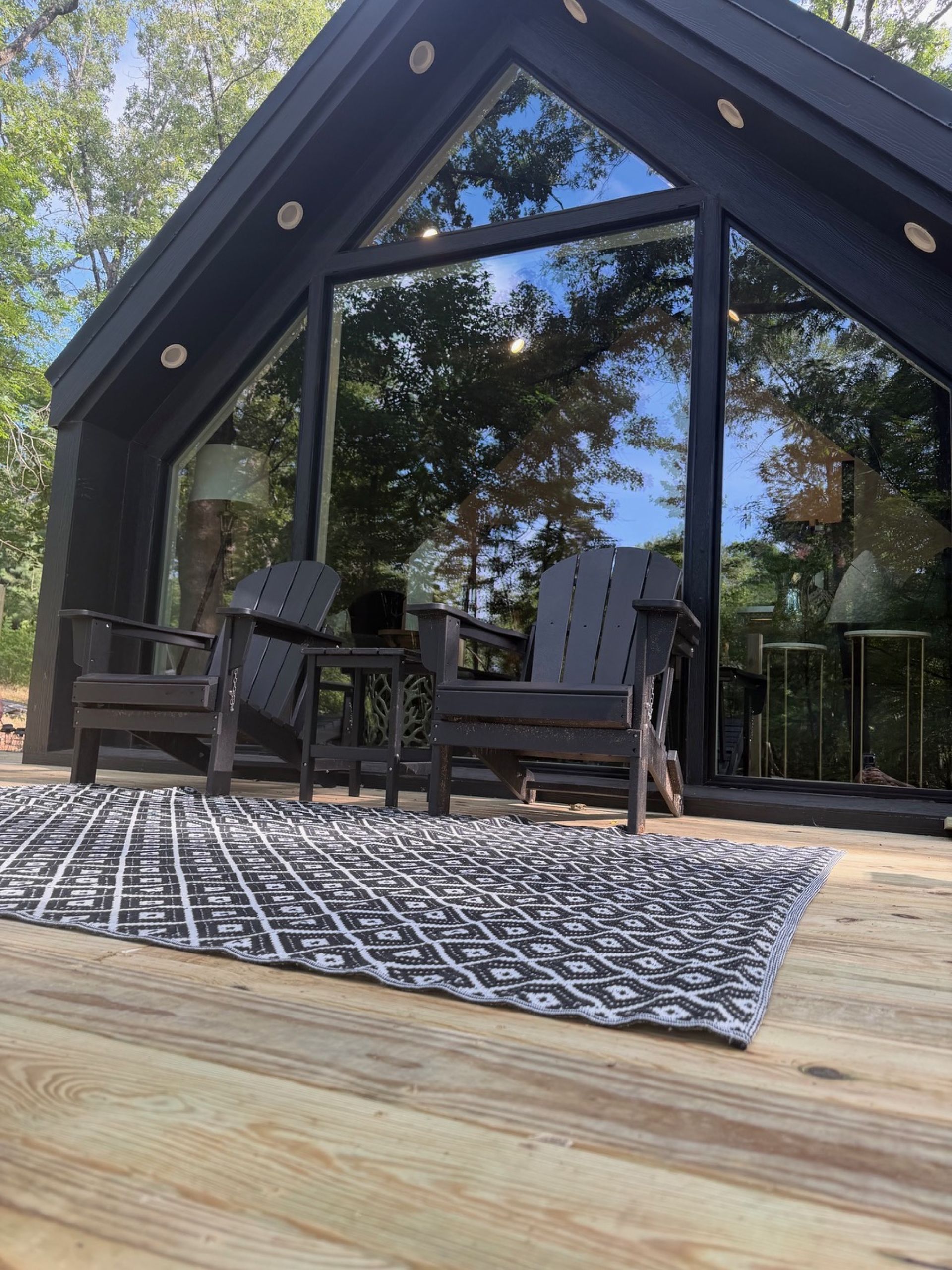 Een modern gebouw met grote ramen, een houten terras en twee Adirondack-stoelen.