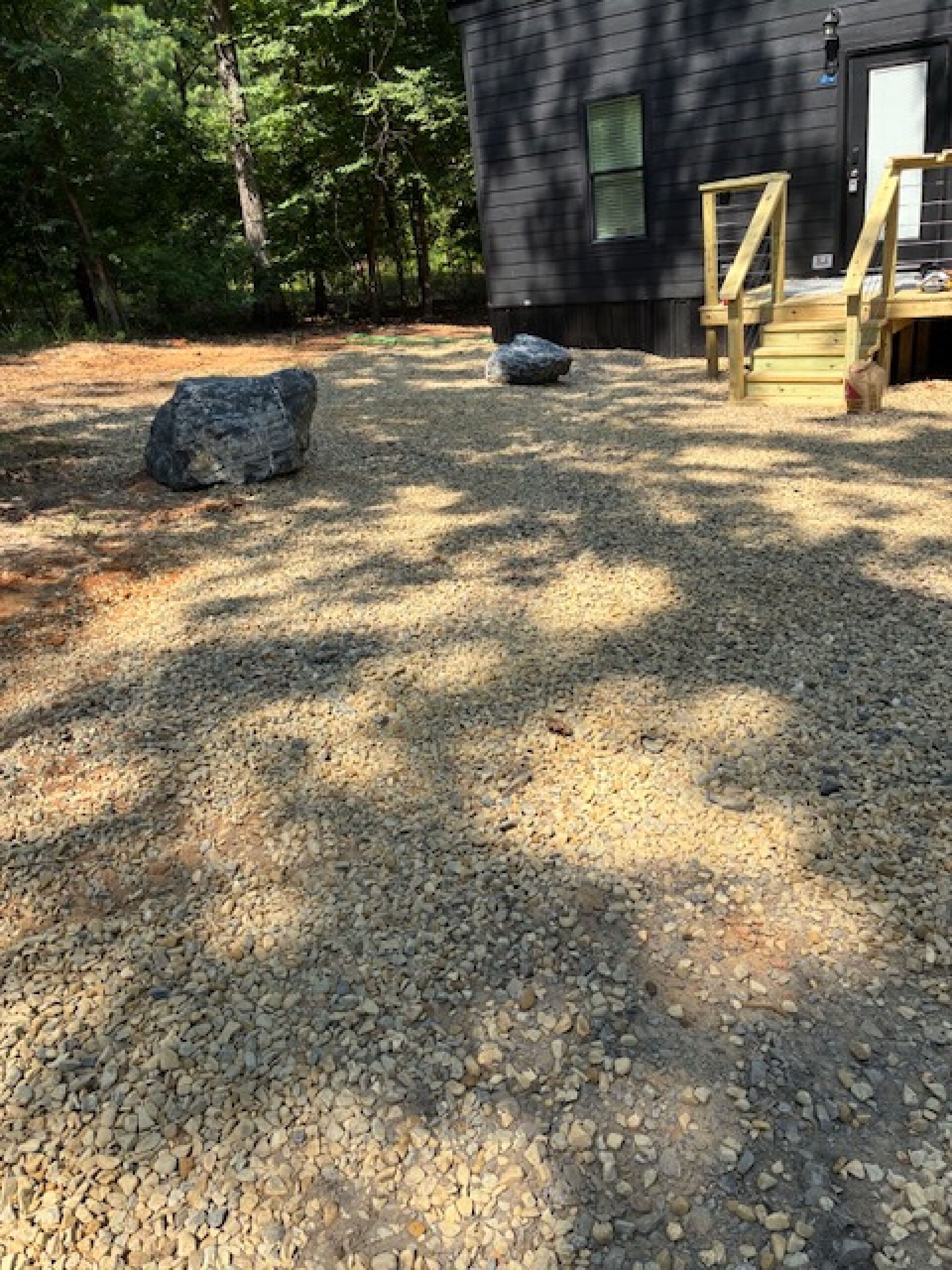 A gravel driveway leading to a wooden deck with a black building in the background.