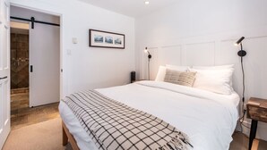 Ein Schlafzimmer mit einem großen Bett, einem gerahmten Bild an der Wand und einer Tür zu einem Badezimmer.
