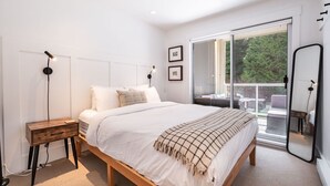Ein modernes Schlafzimmer mit einem großen Bett, einem Nachttisch aus Holz, einer Stehlampe und einer Glastür zum Balkon.