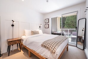 Ein modernes Schlafzimmer mit einem großen Bett, einem Nachttisch aus Holz, einer Stehlampe und einer Glastür zum Balkon.