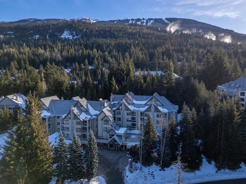 A multi-story lodge with a symmetrical facade, surrounded by snow-covered ground and dense forest.