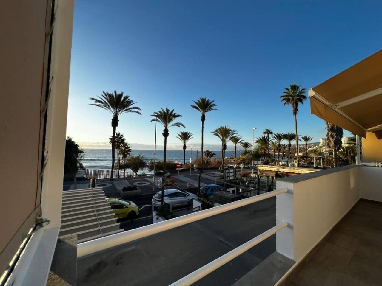 A balcony with a view of a parking area, palm trees, and a body of water.