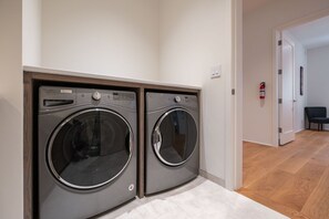 A laundry room with two front-loading Whirlpool washers, a white door, a fire extinguisher, and a chair in the adjacent room. - Ultimate Secluded Chalet | Private hot tub (Whistler)