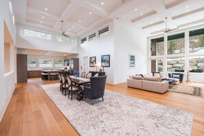 A spacious living area with a dining table, sofa, and large windows offering views of the outdoors. - Ultimate Secluded Chalet | Private hot tub (Whistler)