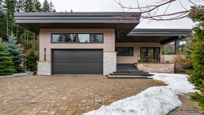 Uma casa moderna de dois andares com garagem, calçada de tijolos e neve acumulada.