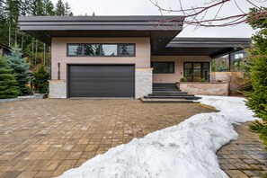 Ein modernes, zweistöckiges Haus mit Garage, Pflasterauffahrt und Schneebedeckung.