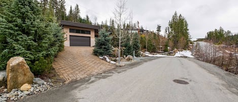 A residential driveway leading to a garage with a brick pathway and a snow-covered landscape.