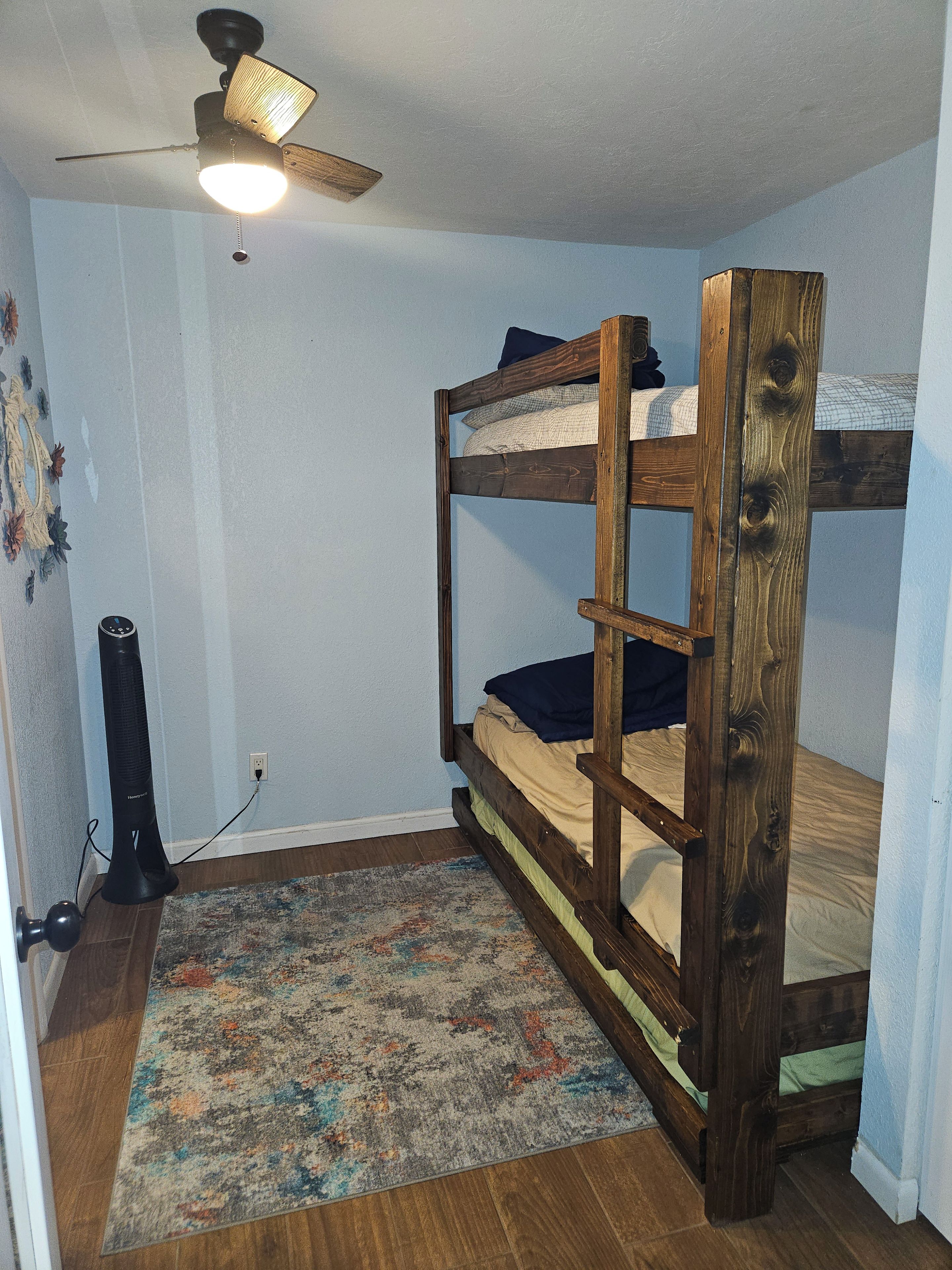 A bunk bed with a ceiling fan, a patterned rug, and a power outlet on the wall.