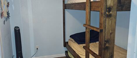 A bunk bed with a ceiling fan, a patterned rug, and a power outlet on the wall.