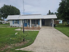 Ein kleines, eingeschossiges Gebäude mit einer überdachten Veranda und einem Betonweg, der zur Eingangstür führt.